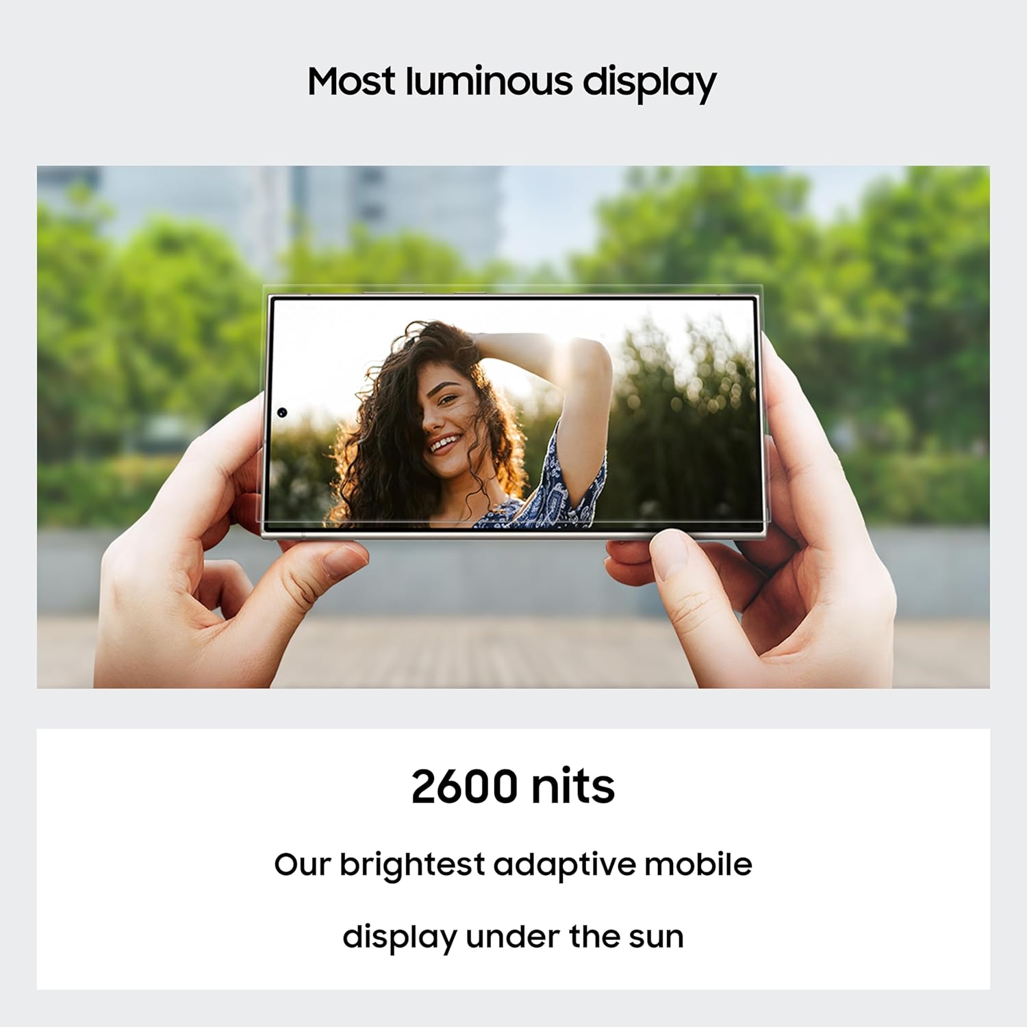 Person holding a smartphone with a woman's face on the screen, outdoors.